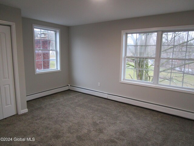 unfurnished bedroom with multiple windows, baseboard heating, and dark carpet