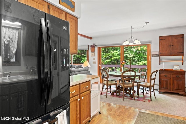 kitchen with light wood-type flooring, pendant lighting, black refrigerator, an inviting chandelier, and sink