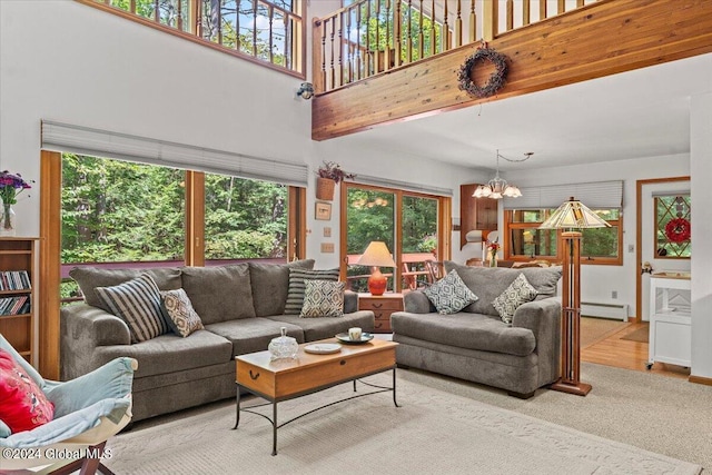 living room with a healthy amount of sunlight, baseboard heating, an inviting chandelier, and light wood-type flooring