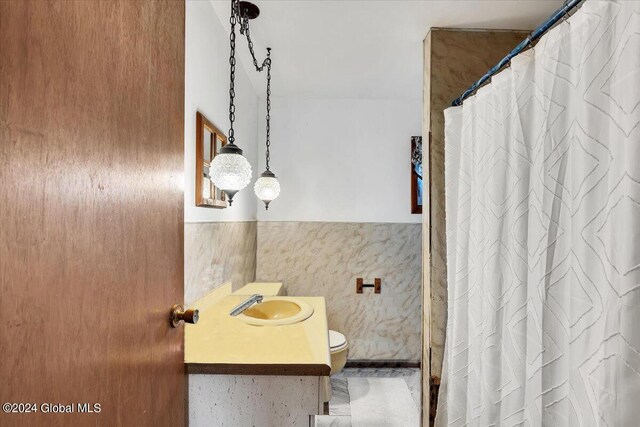 bathroom featuring curtained shower, toilet, a wainscoted wall, vanity, and tile walls