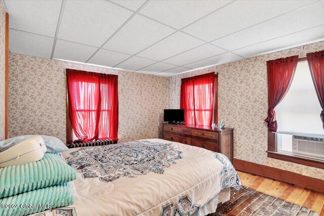 bedroom with cooling unit, a drop ceiling, wood finished floors, and wallpapered walls