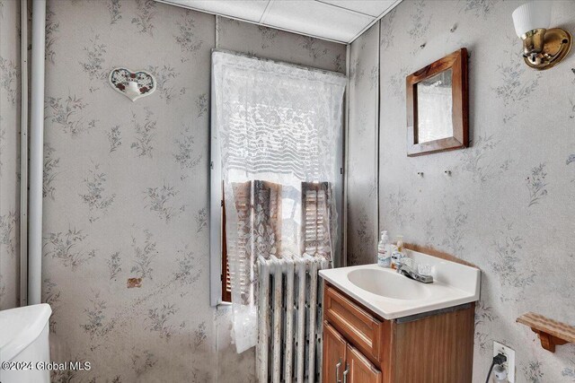 half bathroom featuring radiator heating unit, vanity, toilet, and wallpapered walls