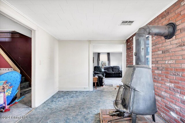 interior space featuring carpet floors, a wood stove, brick wall, and crown molding