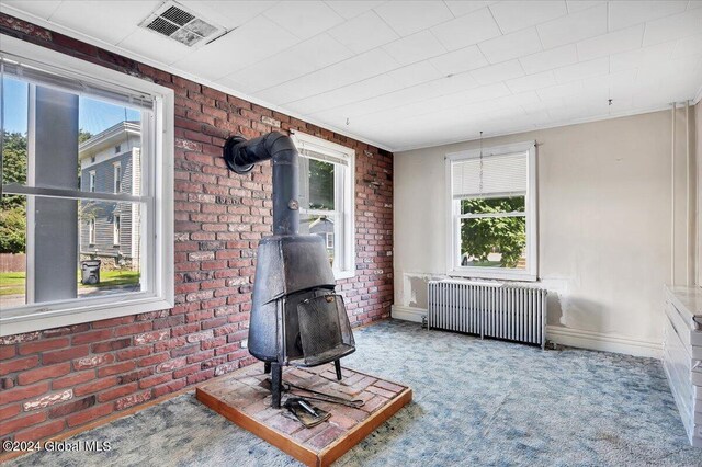 carpeted living room featuring brick wall, visible vents, baseboards, radiator heating unit, and a wood stove