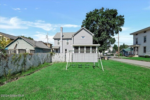 back of property with a yard, a chimney, a shingled roof, a sunroom, and fence