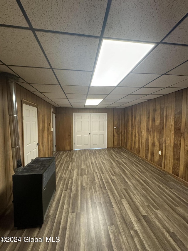 basement featuring a paneled ceiling, wood walls, and dark hardwood / wood-style floors