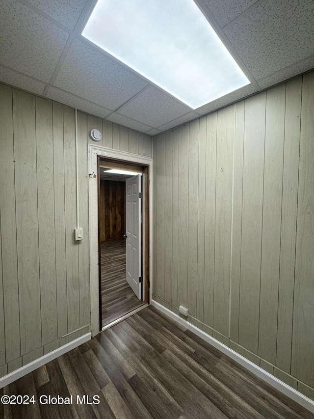 empty room with dark hardwood / wood-style floors, a drop ceiling, and wooden walls