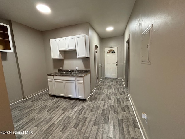 kitchen with electric panel, white cabinets, hardwood / wood-style flooring, and sink