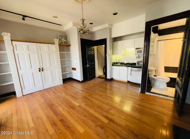 unfurnished bedroom featuring track lighting, light hardwood / wood-style flooring, connected bathroom, and a chandelier