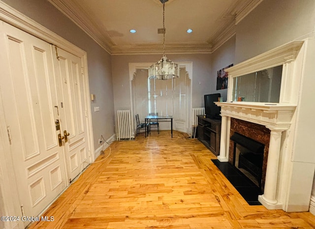 interior space with an inviting chandelier, a premium fireplace, light hardwood / wood-style flooring, ornamental molding, and radiator heating unit