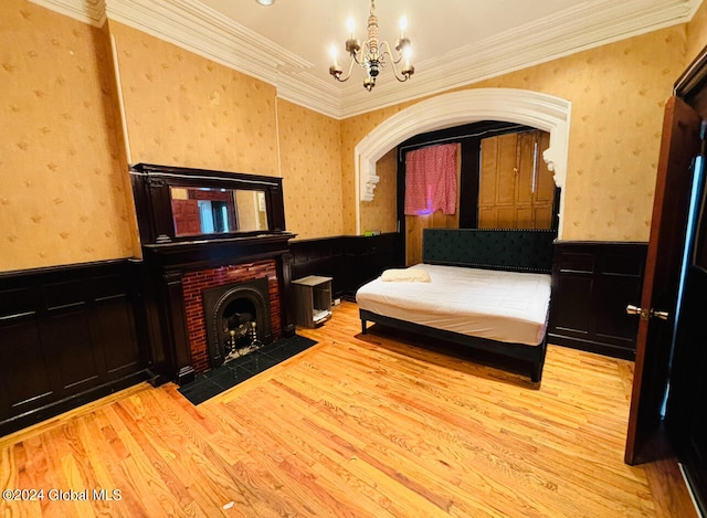 bedroom featuring ornamental molding, a brick fireplace, a notable chandelier, and light hardwood / wood-style floors