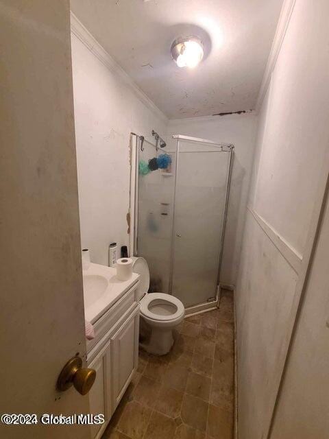 bathroom featuring toilet, vanity, a shower with shower door, and ornamental molding