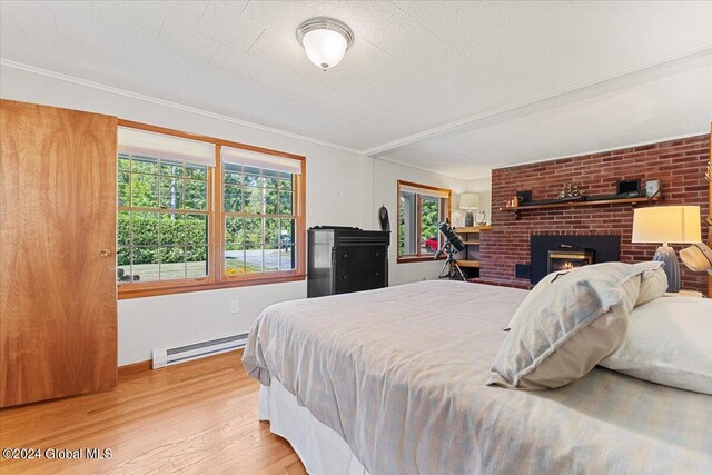 bedroom with a baseboard radiator, a fireplace, ornamental molding, and light hardwood / wood-style flooring