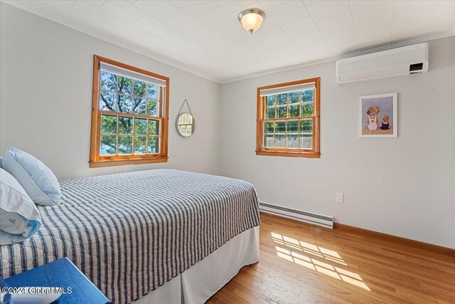 bedroom featuring crown molding, hardwood / wood-style flooring, baseboard heating, and an AC wall unit