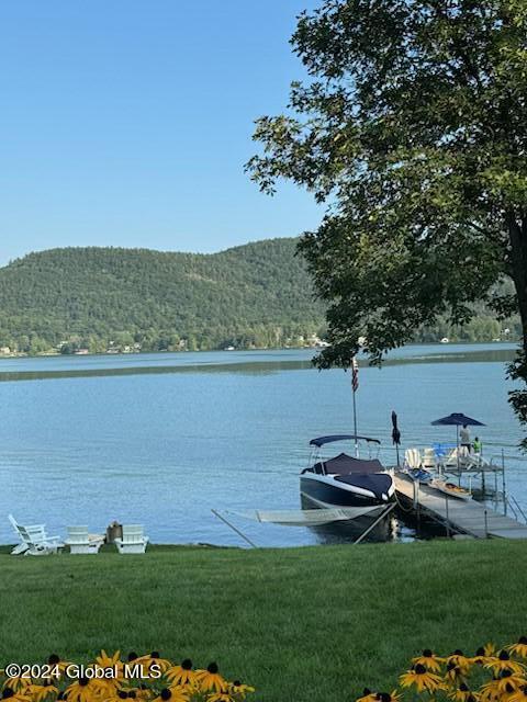 view of dock with a water and mountain view and a lawn