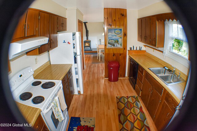 kitchen featuring a wood stove, white appliances, sink, light hardwood / wood-style floors, and range hood