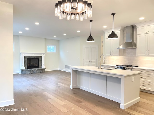 kitchen featuring a chandelier, light hardwood / wood-style floors, sink, wall chimney range hood, and a center island with sink