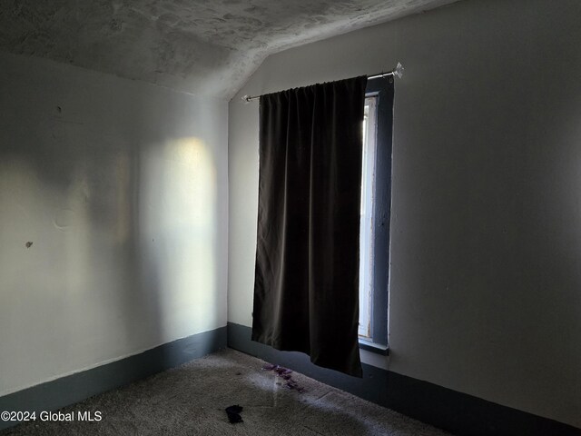 carpeted empty room with vaulted ceiling