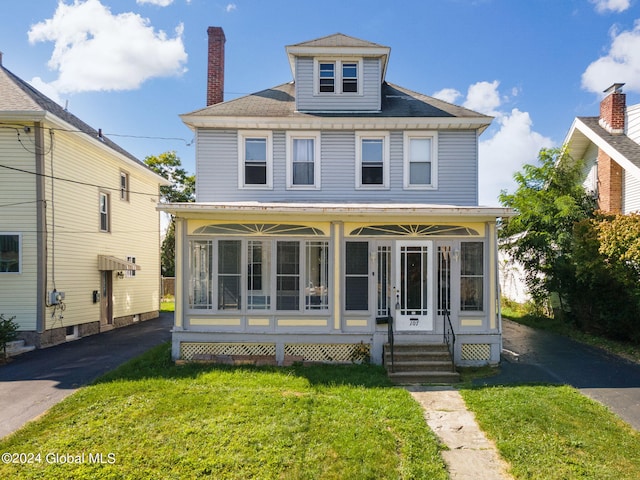 traditional style home featuring entry steps, a front lawn, a sunroom, and a shingled roof