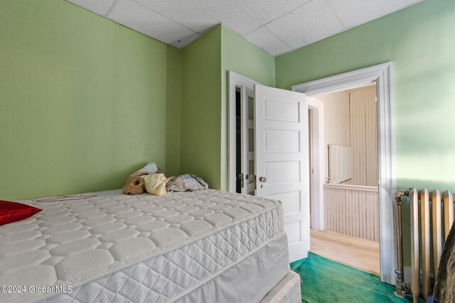 carpeted bedroom with a paneled ceiling and radiator