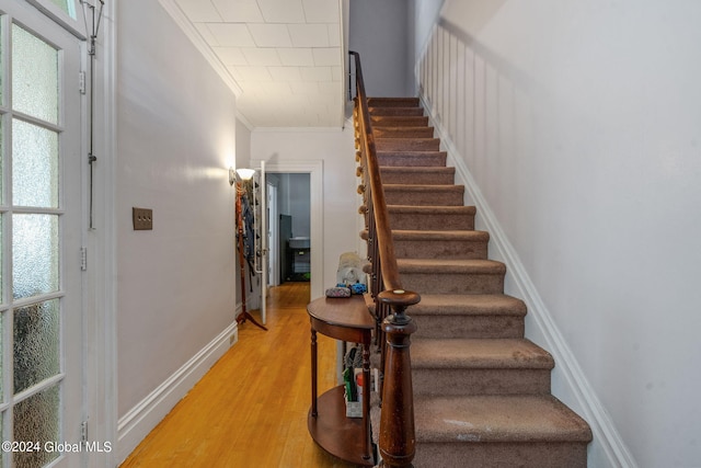 staircase featuring crown molding, a healthy amount of sunlight, and wood-type flooring