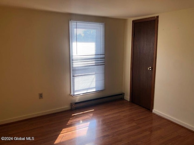 unfurnished room with a baseboard heating unit, a healthy amount of sunlight, baseboards, and wood finished floors