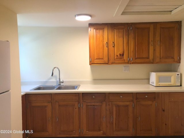 kitchen featuring white microwave, brown cabinets, a sink, and light countertops