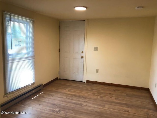 empty room with plenty of natural light, a baseboard radiator, baseboards, and wood finished floors