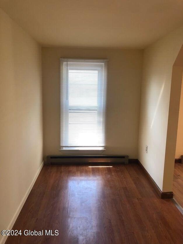 unfurnished room with a baseboard radiator, baseboards, and dark wood-type flooring