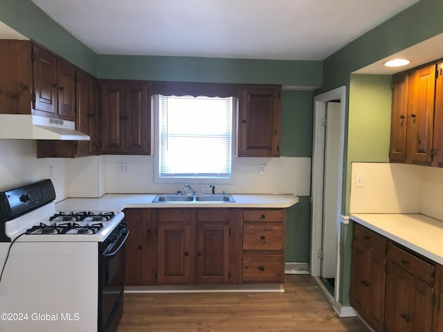 kitchen with under cabinet range hood, wood finished floors, a sink, range with gas stovetop, and light countertops