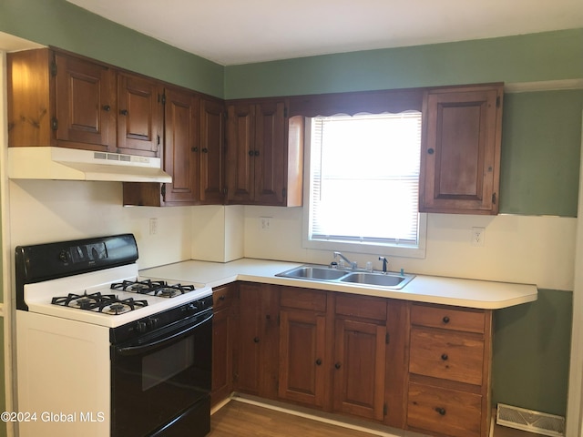 kitchen with range with gas cooktop, wood finished floors, light countertops, under cabinet range hood, and a sink