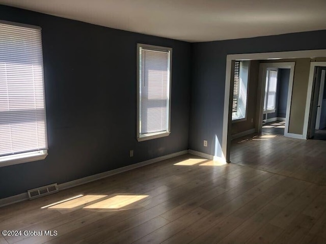 spare room featuring wood-type flooring, visible vents, and baseboards