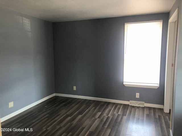 unfurnished room with visible vents, dark wood finished floors, and baseboards