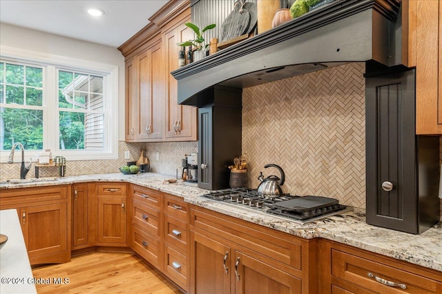 kitchen featuring tasteful backsplash, custom range hood, sink, light hardwood / wood-style flooring, and stainless steel gas stovetop