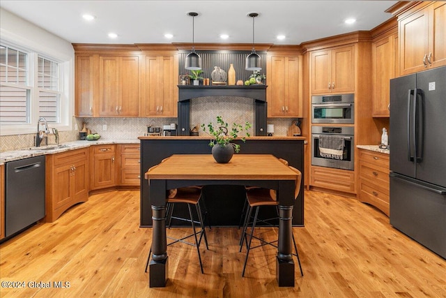 kitchen featuring pendant lighting, light stone counters, light wood-type flooring, and appliances with stainless steel finishes