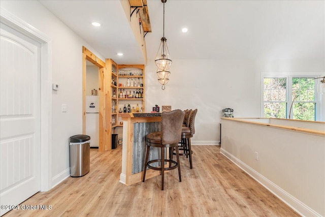 bar featuring light wood-type flooring, white refrigerator, hanging light fixtures, and butcher block counters