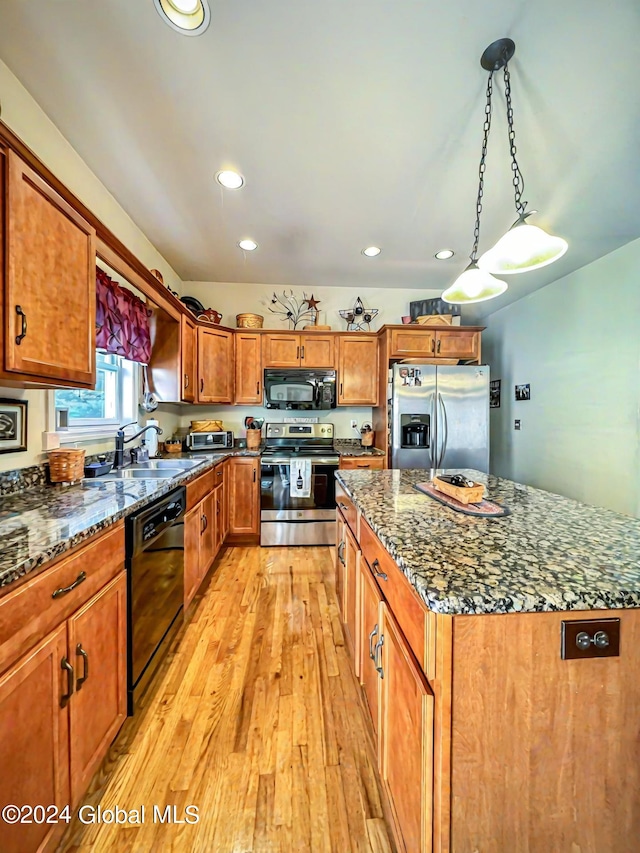 kitchen with decorative light fixtures, black appliances, a center island, sink, and light hardwood / wood-style floors