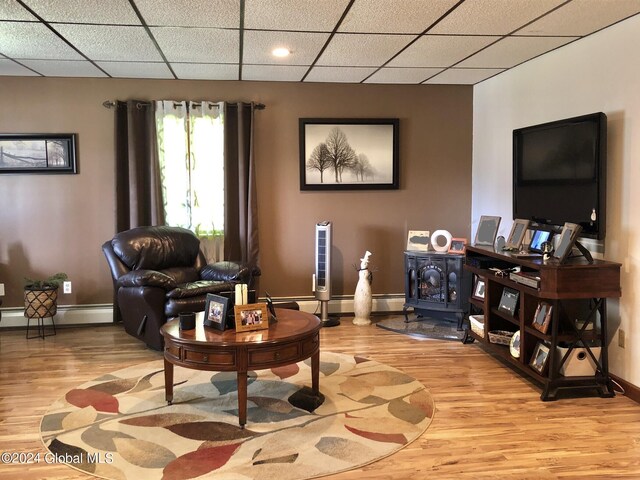 living area featuring baseboard heating, a wood stove, a drop ceiling, and light wood-type flooring