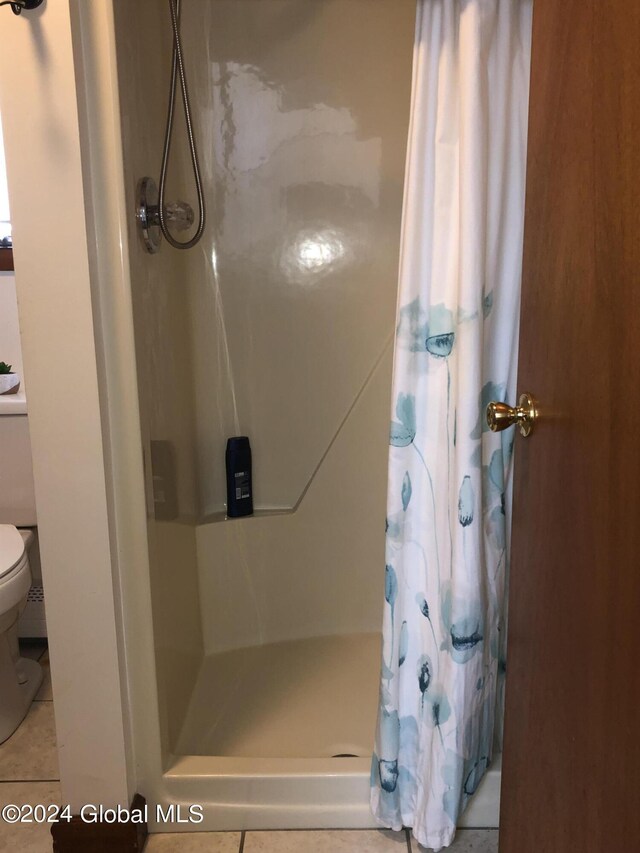 bathroom with toilet, walk in shower, and tile patterned flooring