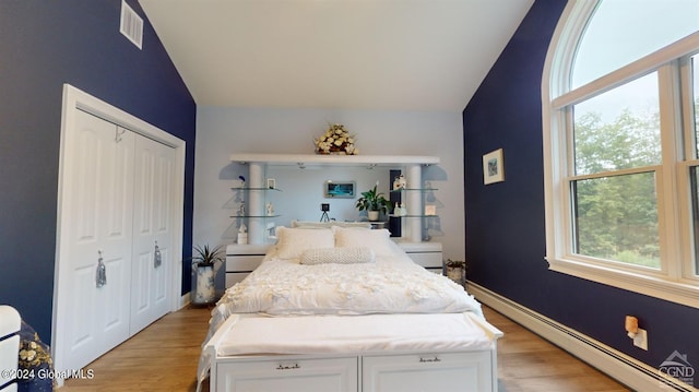 bedroom with light hardwood / wood-style floors, lofted ceiling, a baseboard radiator, and a closet