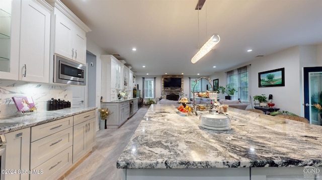 kitchen with white cabinets, decorative light fixtures, a large island, a stone fireplace, and stainless steel microwave