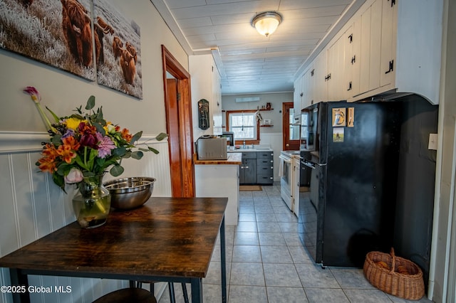 kitchen featuring light tile patterned floors, butcher block counters, white range with electric stovetop, white cabinets, and black fridge