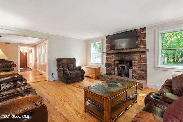 living room featuring ornamental molding, light wood-type flooring, a brick fireplace, and an inviting chandelier