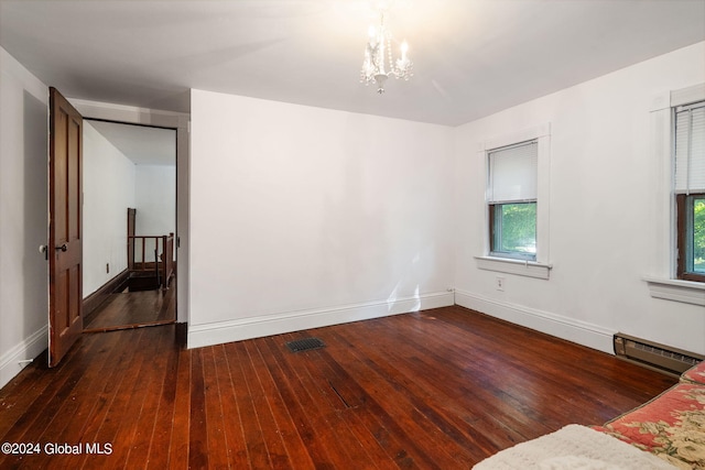 empty room with dark wood-type flooring, baseboard heating, a chandelier, and a wealth of natural light