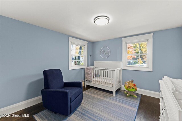 bedroom featuring dark hardwood / wood-style flooring, a nursery area, and multiple windows