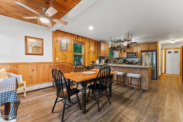 dining room featuring sink, wooden walls, wood-type flooring, and ceiling fan