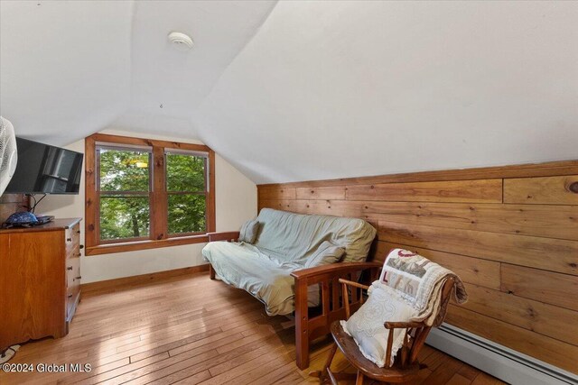 living area featuring baseboard heating, light hardwood / wood-style floors, and vaulted ceiling