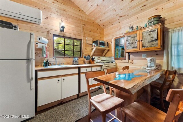 kitchen featuring an AC wall unit, white cabinetry, appliances with stainless steel finishes, wooden walls, and lofted ceiling