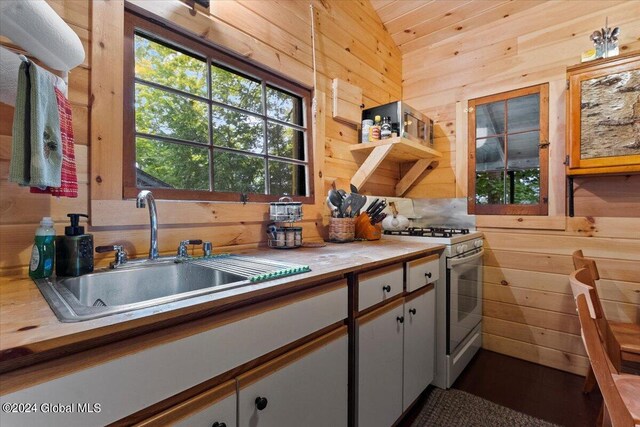 kitchen featuring white gas range, white cabinetry, sink, lofted ceiling, and wooden walls