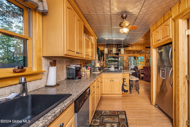 kitchen with sink, wooden walls, stone counters, light hardwood / wood-style flooring, and stainless steel appliances